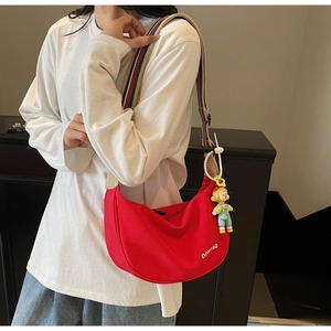 Macro shot of red canvas crescent bag with colorful wide strap and cute doll pendant