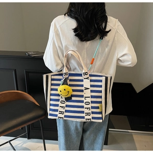 Detail of blue striped canvas tote bag with letter handle and yellow smiley face charm