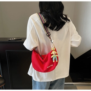 Detail of red canvas dumpling bag with a striped strap and cute cartoon doll pendant