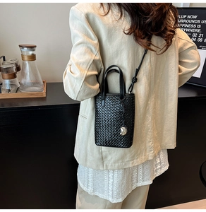 Dettaglio della mini borsa tote nera intrecciata con ciondolo a cuore sul modello