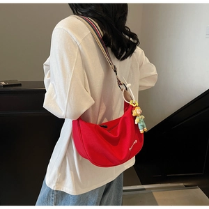 Detail of red crescent bag with colorful striped strap and cartoon pendant on person