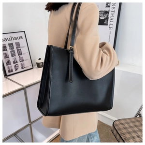 Detail of minimalist black tote bag featuring white contrast stitching and adjustable straps