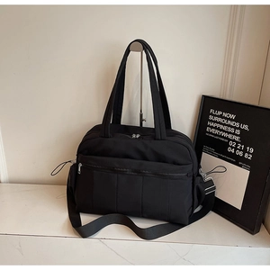 Detail of black nylon travel tote featuring a front zipper pocket and adjustable shoulder strap