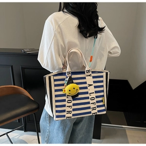 Macro detail of blue striped canvas tote bag featuring lettered straps and yellow smiley charm