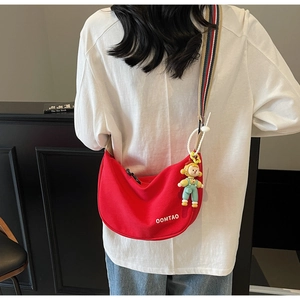 Detail of red canvas half-moon bag with wide striped strap and cartoon pendant