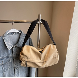 Close-up of khaki nylon crossbody bag on metal stand with a casual denim jacket background