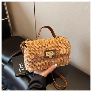 Detail of hand-woven straw bag featuring brown leather handle and gold twist-lock closure