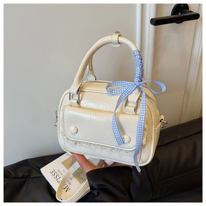 Detail of cream glossy leather handbag with lace trim and blue gingham ribbon bow