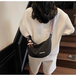 Detail of black crescent crossbody bag with tricolor strap and doll pendant worn by model
