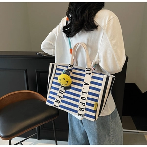 Detail of blue and white striped tote bag with lettered strap and yellow smiley charm