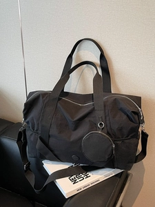 Große schwarze Nylon-Reisetasche mit Schultergurt und kleiner Geldbörse auf dem Sofa