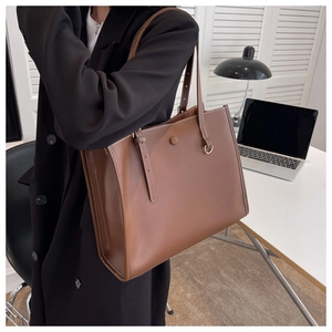 Close-up of brown tote bag showing contrast white stitching and decorative metal buckle
