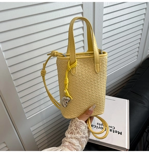 Dettaglio della mini borsa a secchiello gialla intrecciata con ciondolo in metallo