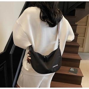 Rear view of black canvas crescent bag with striped strap and doll pendant detail
