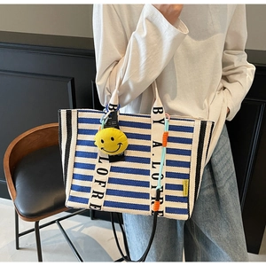 Close-up of striped canvas tote bag with lettered shoulder strap and yellow smiley charm