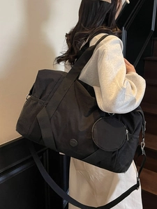 Große schwarze Reisetasche mit rundem Anhänger und verstellbarem Schultergurt an einem Model