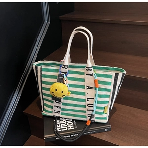 Detail of green striped canvas tote bag featuring lettered straps and yellow smiley charm