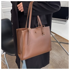 Close-up of brown leather tote bag showing white contrast stitching and gold ring details