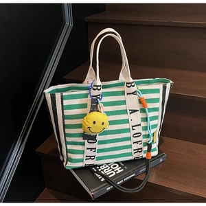 Detail of green striped canvas tote bag with lettered handles and yellow smiley charm