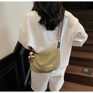 Detail view of olive green crescent bag with striped strap and a cute doll charm
