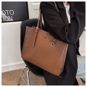 Detail of a brown leather tote bag with white contrast stitching and adjustable straps