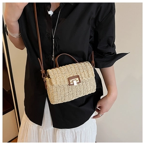 Detail of woven straw handbag with brown leather handles and metal twist lock closure
