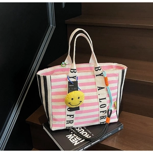 Detail of pink striped tote bag with black lettered handles and plush smiley charm