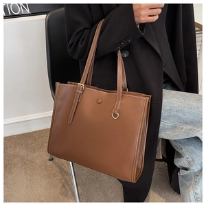 Detail of a large brown tote bag showing white double stitching and metallic D-ring