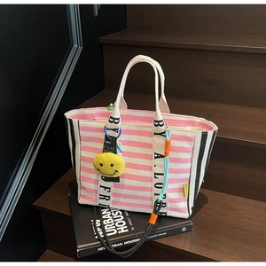 Close-up of pink striped canvas tote bag with a yellow smiley face charm and wide handles