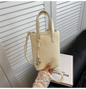 Dettaglio della borsa a secchiello intrecciata beige con ciondolo a cuore e nodo laterale