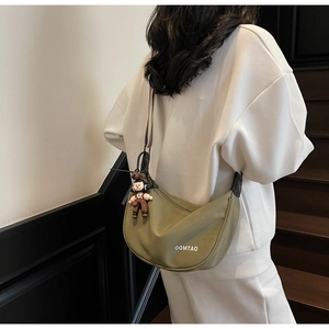 Olive green crescent bag featuring a striped wide strap and a cute cartoon charm