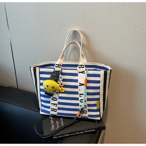 Detail of striped tote bag with dual handles and colorful beaded smiley face charm accessory