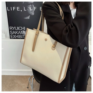 Side view of a large cream leather tote bag with brown handles and metal detail on shoulder