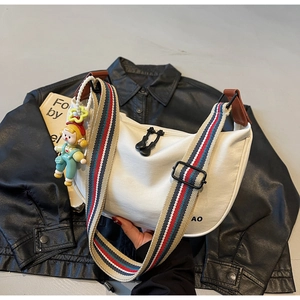 Detail of white canvas dumpling bag featuring colorful striped strap and cartoon pendant