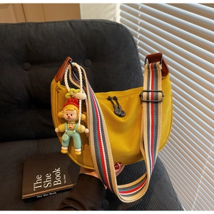 Detail of a bright yellow crescent bag with wide striped strap and cartoon doll charm