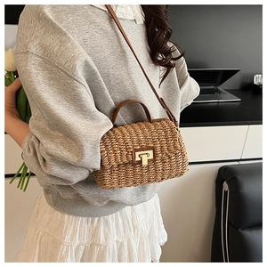 Detail view of woven straw bag with brown leather handles and gold lock worn by a model