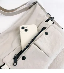 Detail of cream multi-pocket crossbody bag showing smartphone storage and utility