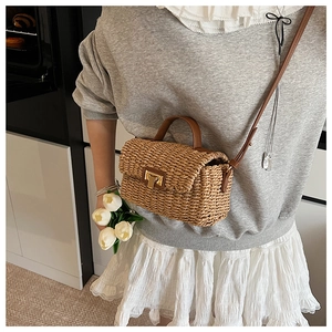 Detail view of woven straw crossbody bag with brown leather handles and gold metal clasp