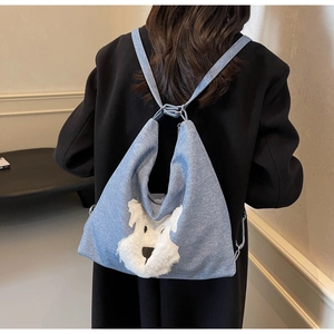 Close-up of light blue denim backpack with a 3D plush dog design on a black coat