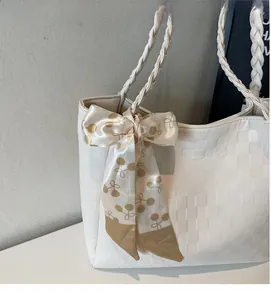 Detailoverzicht van witte geruite draagtas met gevlochten handvatten en kersenzijden sjaal