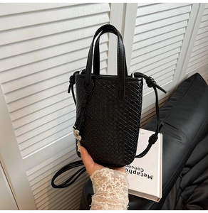 Dettaglio di una borsa tote nera intrecciata con tracolla a nodo regolabile e trama a incrocio
