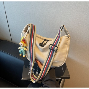 Detail of beige crescent bag featuring colorful striped wide strap and cute charm