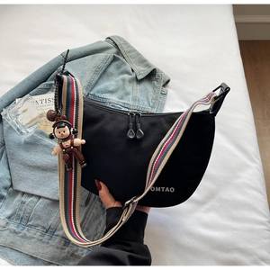 Detail of black nylon dumpling bag with colorful striped strap and cartoon doll pendant