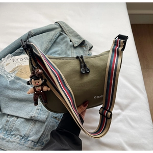 Detail of army green canvas dumpling bag with colorful striped strap and cartoon pendant