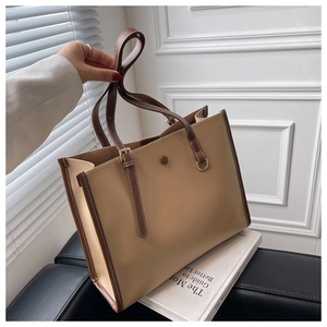 Detail of contrast stitch tote bag with brown leather trim and golden metal buckles