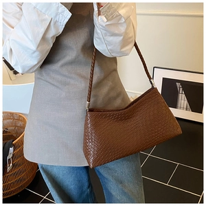 Détail de la texture tressée marron foncé et des anneaux métalliques sur un sac chic