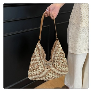 Detail of woven straw tote bag featuring contrast stitching and leather shoulder strap