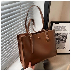 Detail of a brown leather tote bag with white contrast stitching and magnetic buckle closure