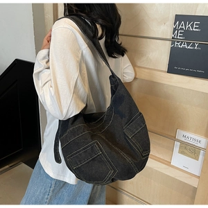 Detail of a large denim crossbody bag with multi-pockets and contrast stitching on the strap