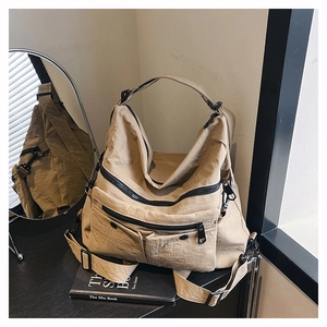 Detail of khaki nylon tote bag showing multiple zipper pockets and wrinkled texture